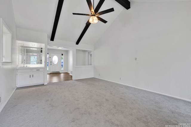 unfurnished living room with ceiling fan, light colored carpet, beamed ceiling, sink, and high vaulted ceiling