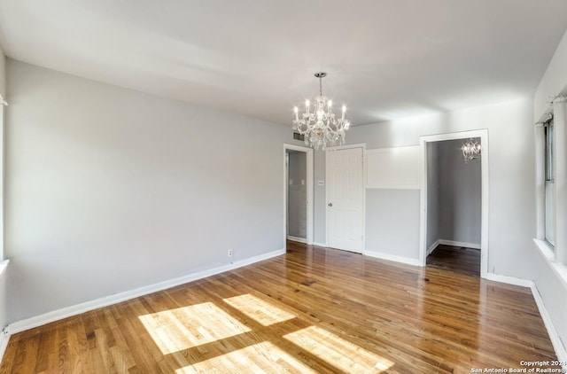 empty room with wood-type flooring and a notable chandelier