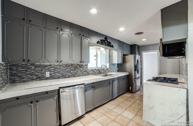 kitchen featuring light tile patterned floors, appliances with stainless steel finishes, gray cabinetry, tasteful backsplash, and sink