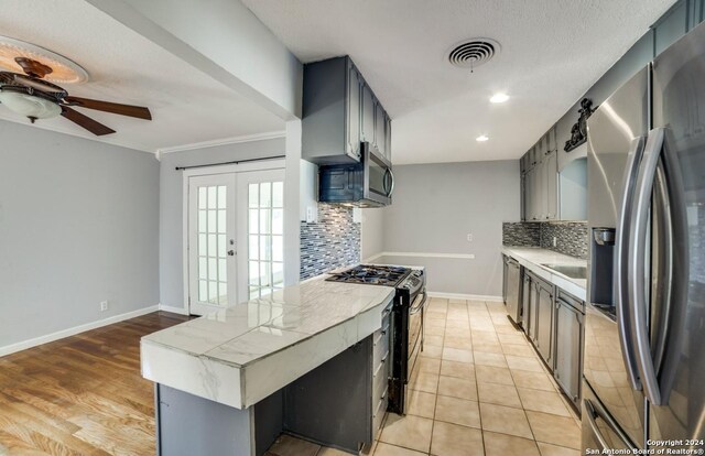 kitchen featuring gray cabinets, ceiling fan, appliances with stainless steel finishes, backsplash, and french doors