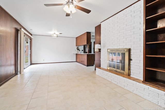 unfurnished living room featuring ceiling fan, built in features, wood walls, a brick fireplace, and light tile patterned floors