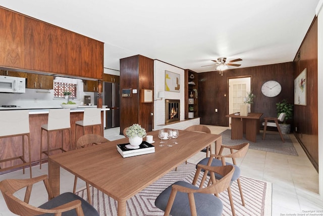 dining room featuring ceiling fan, a fireplace, wooden walls, built in features, and light tile patterned floors