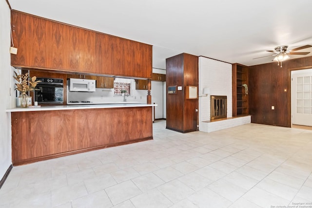 kitchen featuring kitchen peninsula, ceiling fan, a brick fireplace, white appliances, and sink