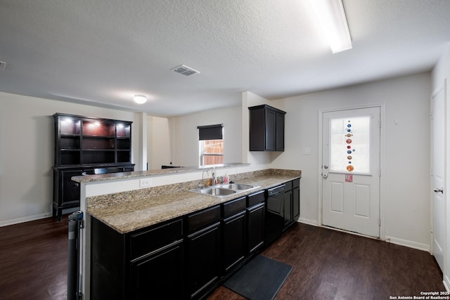 kitchen with kitchen peninsula, dark wood-type flooring, light stone countertops, a textured ceiling, and sink