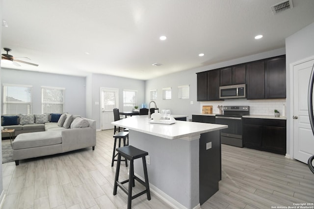 kitchen with an island with sink, ceiling fan, stainless steel appliances, tasteful backsplash, and a breakfast bar