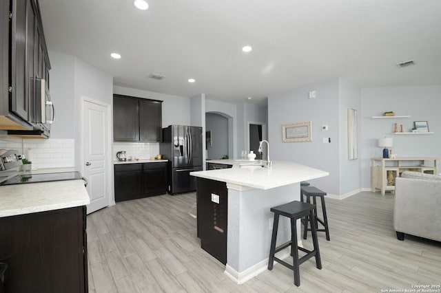 kitchen featuring an island with sink, appliances with stainless steel finishes, decorative backsplash, light hardwood / wood-style flooring, and a breakfast bar