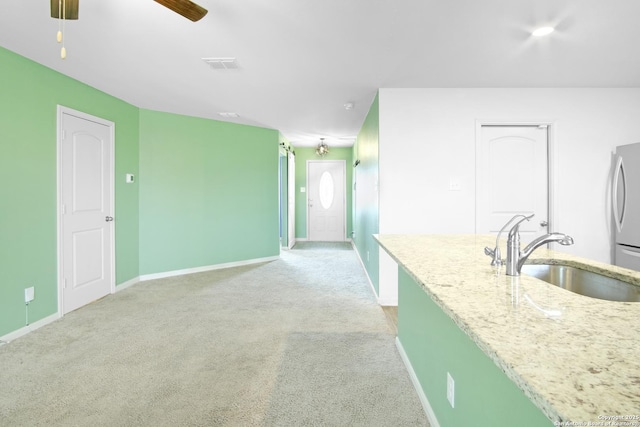 kitchen featuring ceiling fan, light colored carpet, sink, stainless steel refrigerator, and light stone counters