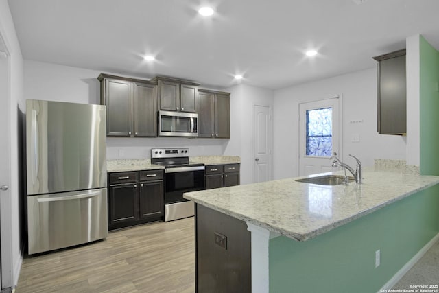 kitchen featuring light hardwood / wood-style floors, kitchen peninsula, sink, light stone countertops, and stainless steel appliances