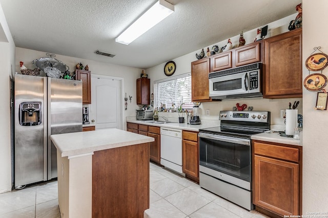 kitchen featuring a textured ceiling, appliances with stainless steel finishes, a center island, sink, and light tile patterned flooring