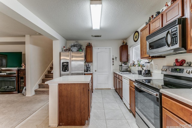 kitchen with appliances with stainless steel finishes, light colored carpet, a textured ceiling, a kitchen island, and sink