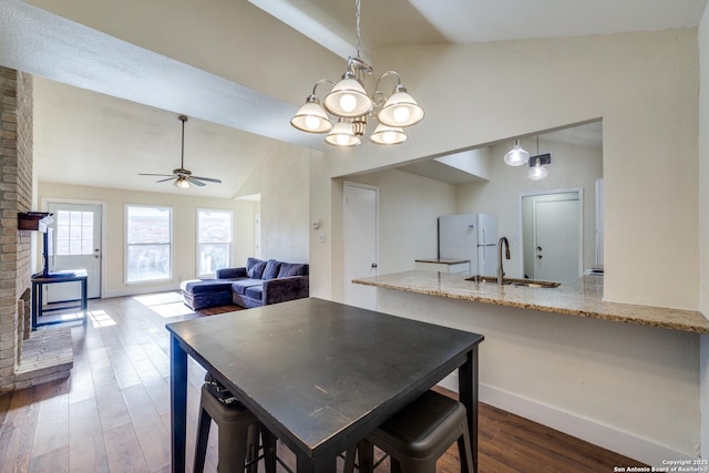 dining area with sink, vaulted ceiling, a wood stove, dark hardwood / wood-style floors, and ceiling fan with notable chandelier