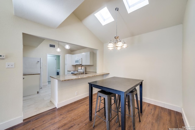 dining space with dark wood-type flooring, a chandelier, and vaulted ceiling with skylight