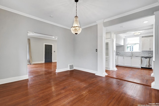 empty room featuring a notable chandelier, hardwood / wood-style floors, sink, ornamental molding, and decorative columns