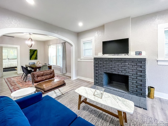 living room with light wood-type flooring, a brick fireplace, and an inviting chandelier