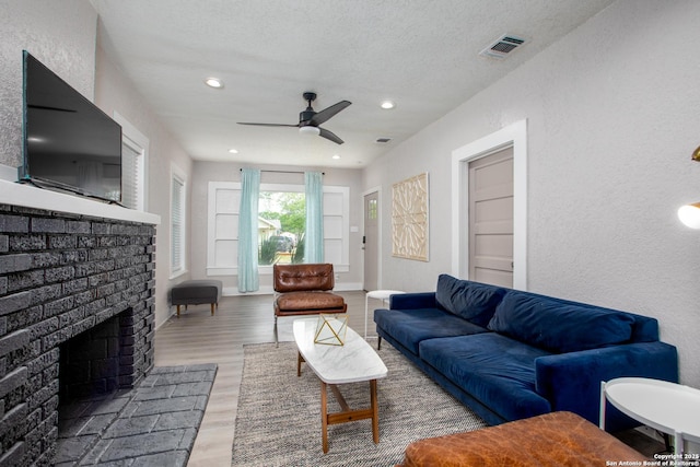 living room with a textured ceiling, ceiling fan, a fireplace, and hardwood / wood-style flooring