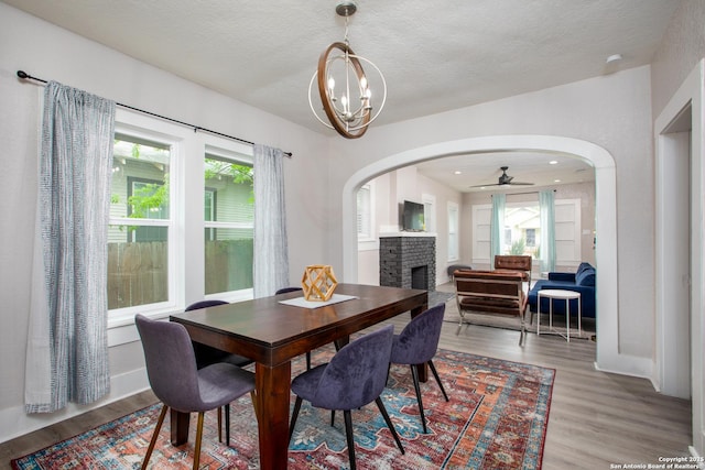 dining area with ceiling fan with notable chandelier, a textured ceiling, light wood-type flooring, and a fireplace