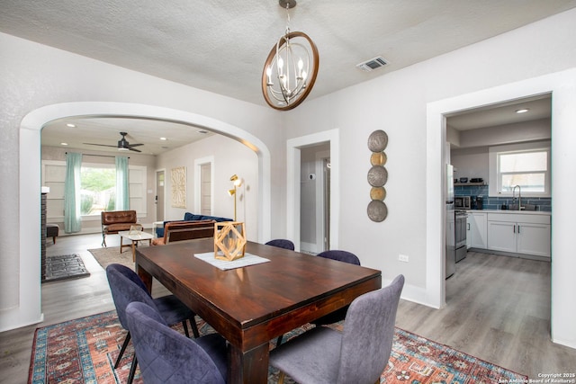 dining space with sink, ceiling fan with notable chandelier, a textured ceiling, and light hardwood / wood-style flooring