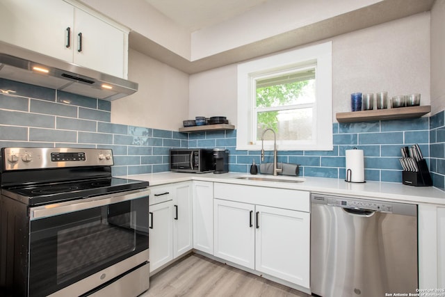 kitchen with range hood, light hardwood / wood-style floors, sink, appliances with stainless steel finishes, and white cabinets