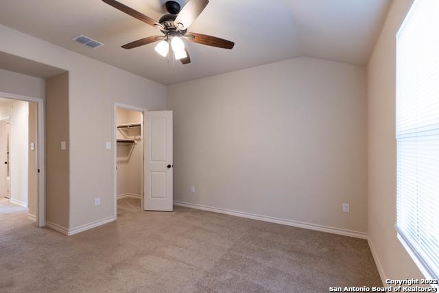 unfurnished bedroom featuring ceiling fan, vaulted ceiling, multiple windows, a spacious closet, and a closet