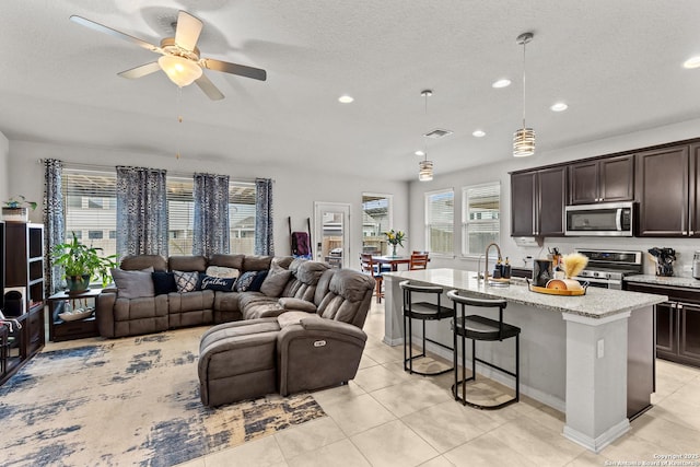 living room with a textured ceiling, ceiling fan, light tile patterned floors, and plenty of natural light