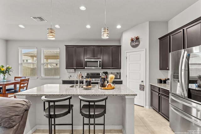 kitchen featuring stainless steel appliances, a kitchen island with sink, hanging light fixtures, light stone counters, and sink