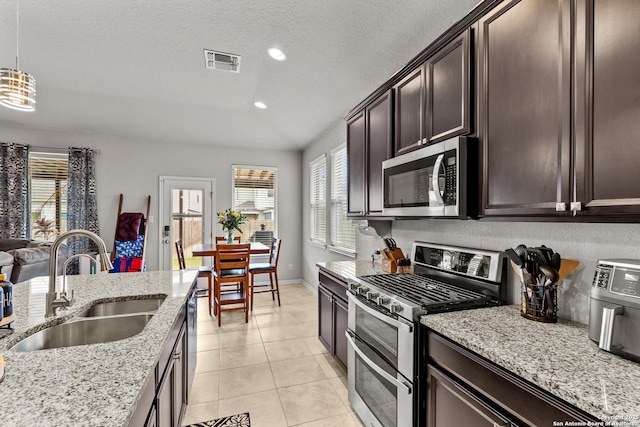 kitchen with a textured ceiling, stainless steel appliances, sink, hanging light fixtures, and dark brown cabinets