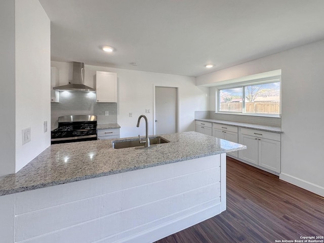 kitchen featuring stainless steel gas stove, wall chimney exhaust hood, white cabinets, light stone counters, and sink