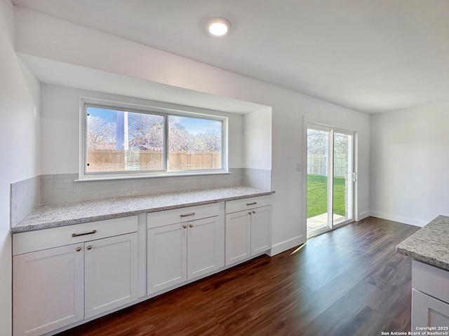 kitchen with light stone counters, plenty of natural light, white cabinets, and dark wood-type flooring