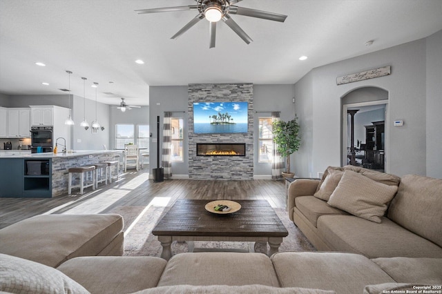 living room featuring a healthy amount of sunlight, light hardwood / wood-style flooring, a stone fireplace, and sink