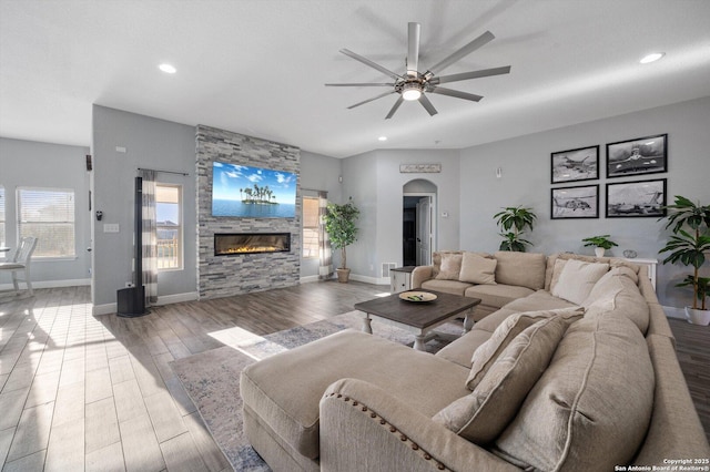 living room with ceiling fan, wood-type flooring, and a stone fireplace