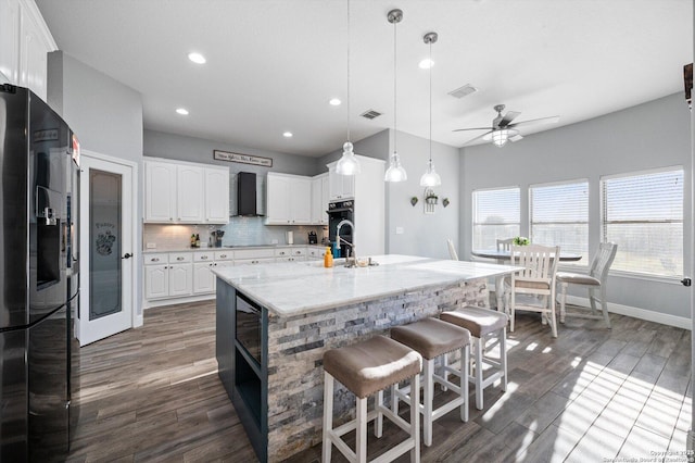 kitchen with a center island with sink, ceiling fan, wall chimney range hood, white cabinets, and black appliances