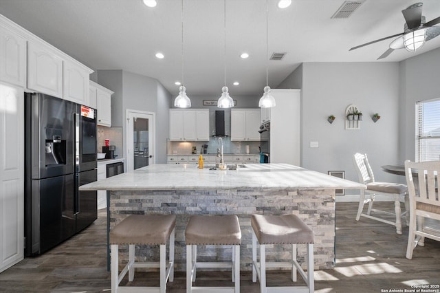 kitchen featuring refrigerator with ice dispenser, decorative light fixtures, white cabinetry, decorative backsplash, and a kitchen island with sink