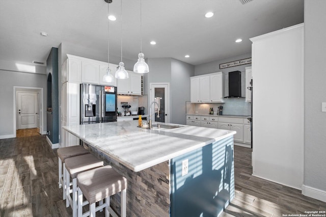 kitchen featuring stainless steel fridge with ice dispenser, a center island with sink, tasteful backsplash, wall chimney exhaust hood, and white cabinets