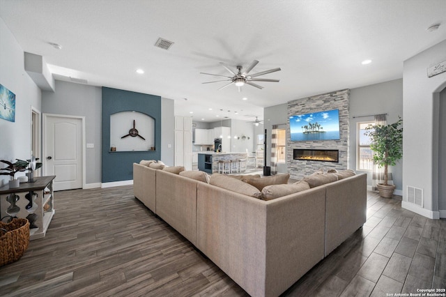 living room featuring a fireplace, ceiling fan, and dark wood-type flooring