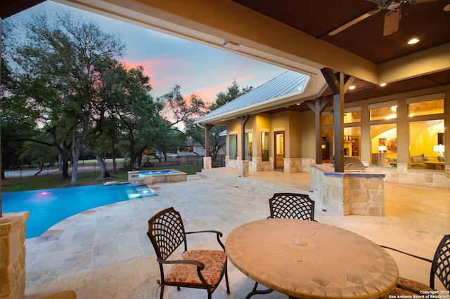 pool at dusk with a bar, ceiling fan, exterior kitchen, an in ground hot tub, and a patio