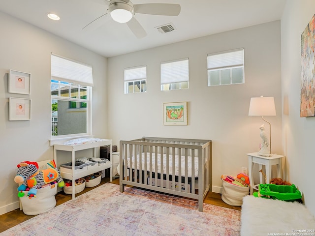 bedroom featuring ceiling fan, hardwood / wood-style flooring, and a crib