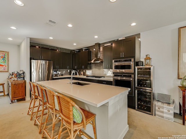 kitchen featuring wall chimney range hood, sink, a kitchen island with sink, a breakfast bar area, and stainless steel appliances