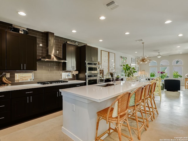 kitchen featuring decorative light fixtures, sink, a kitchen island with sink, a breakfast bar area, and wall chimney exhaust hood