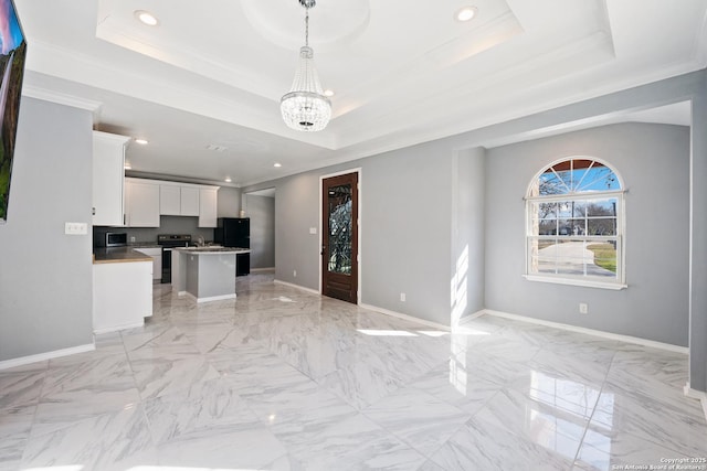 unfurnished living room with a tray ceiling, crown molding, and an inviting chandelier