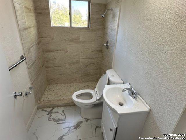 bathroom with toilet, tiled shower, and vanity