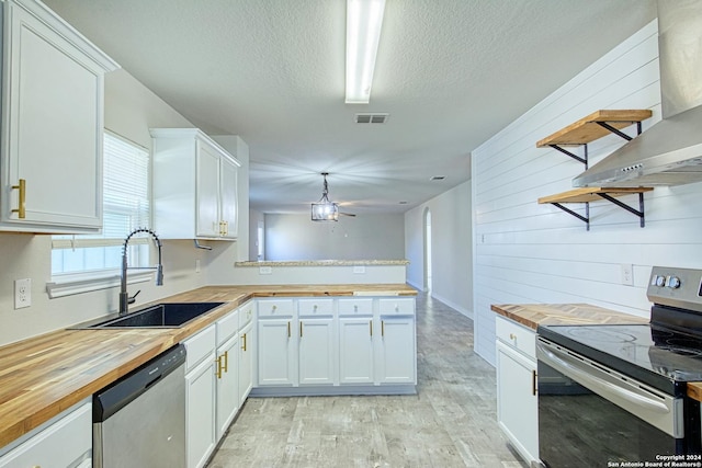 kitchen with wood walls, sink, white cabinetry, stainless steel appliances, and butcher block counters