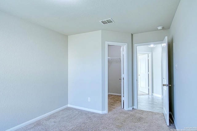 unfurnished bedroom featuring a spacious closet, light colored carpet, and a closet