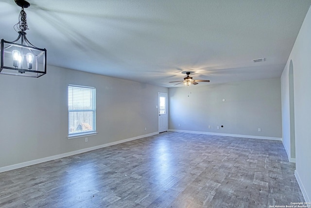 empty room with a textured ceiling, wood-type flooring, ceiling fan with notable chandelier, and plenty of natural light