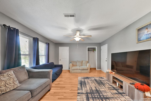 living room with ceiling fan, a textured ceiling, and light hardwood / wood-style floors