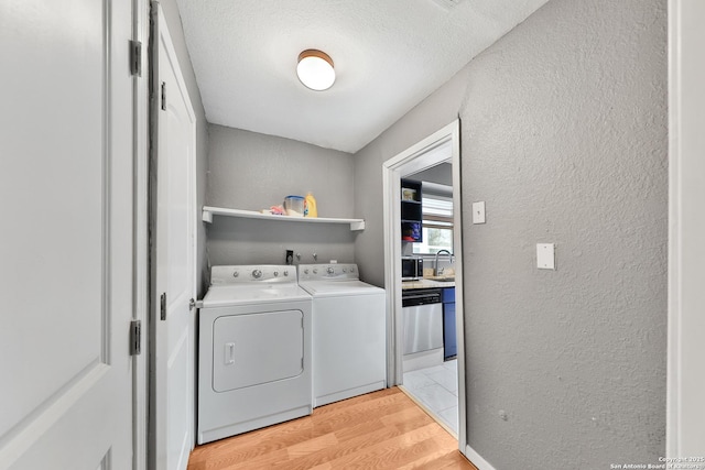 laundry room with light hardwood / wood-style floors, sink, a textured ceiling, and washing machine and clothes dryer