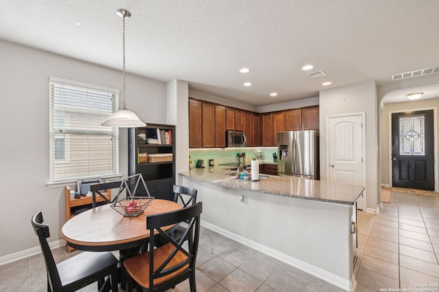 kitchen with light tile patterned floors, kitchen peninsula, stainless steel appliances, hanging light fixtures, and a textured ceiling