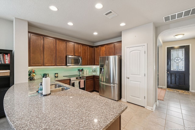 kitchen featuring kitchen peninsula, sink, light tile patterned flooring, light stone countertops, and appliances with stainless steel finishes