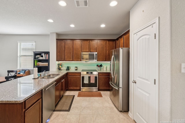 kitchen with kitchen peninsula, appliances with stainless steel finishes, light tile patterned flooring, light stone counters, and sink