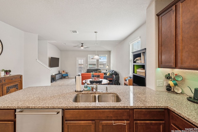 kitchen with ceiling fan, kitchen peninsula, light stone counters, and sink