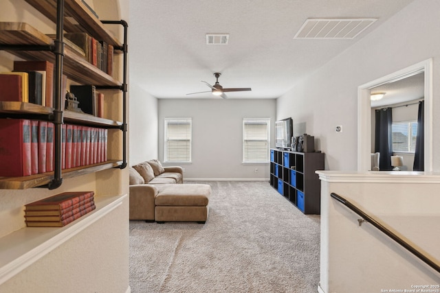 living area featuring ceiling fan, light colored carpet, plenty of natural light, and a textured ceiling